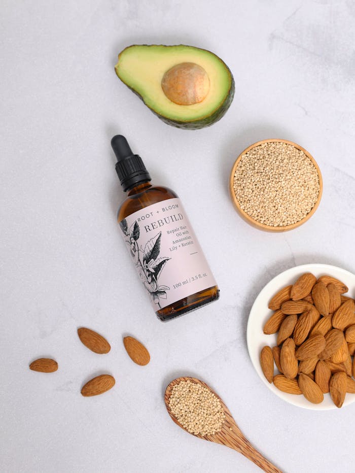 Flat lay of natural hair oil with almonds, avocado, quinoa, and seeds for hair health.