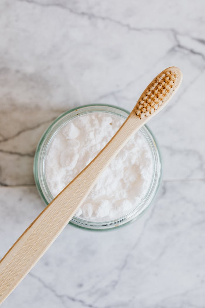 Top view of wooden toothbrush placed over glass jar of tooth powder on marble surface