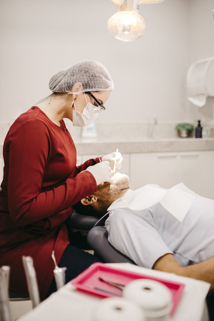 Side view of anonymous female stomatologist in eyeglasses and gloves checking teeth of lying man in clinic